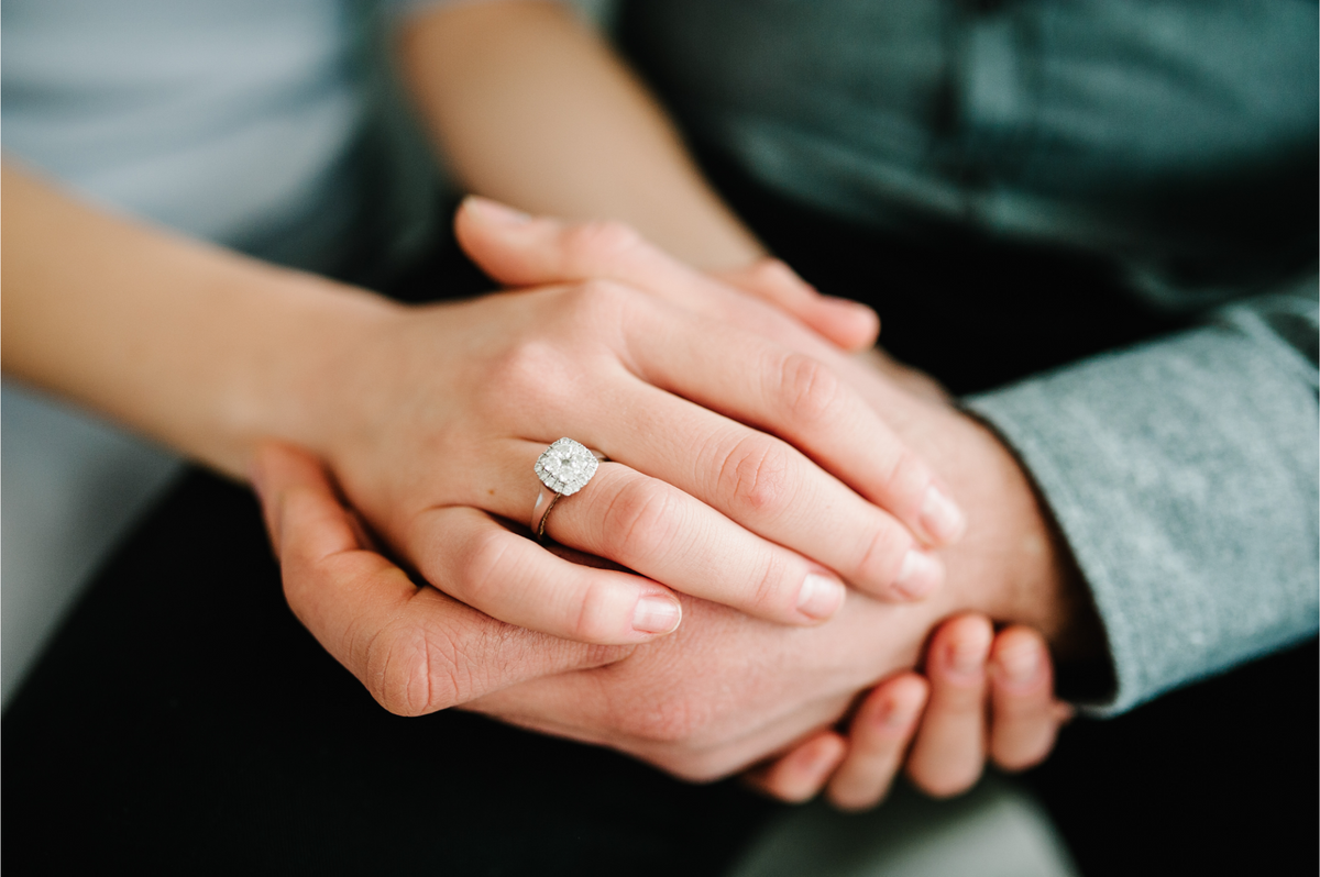 tightly cropped view of a couple holding hands, with a woman's hand featuring a large diamond engagement ring on top