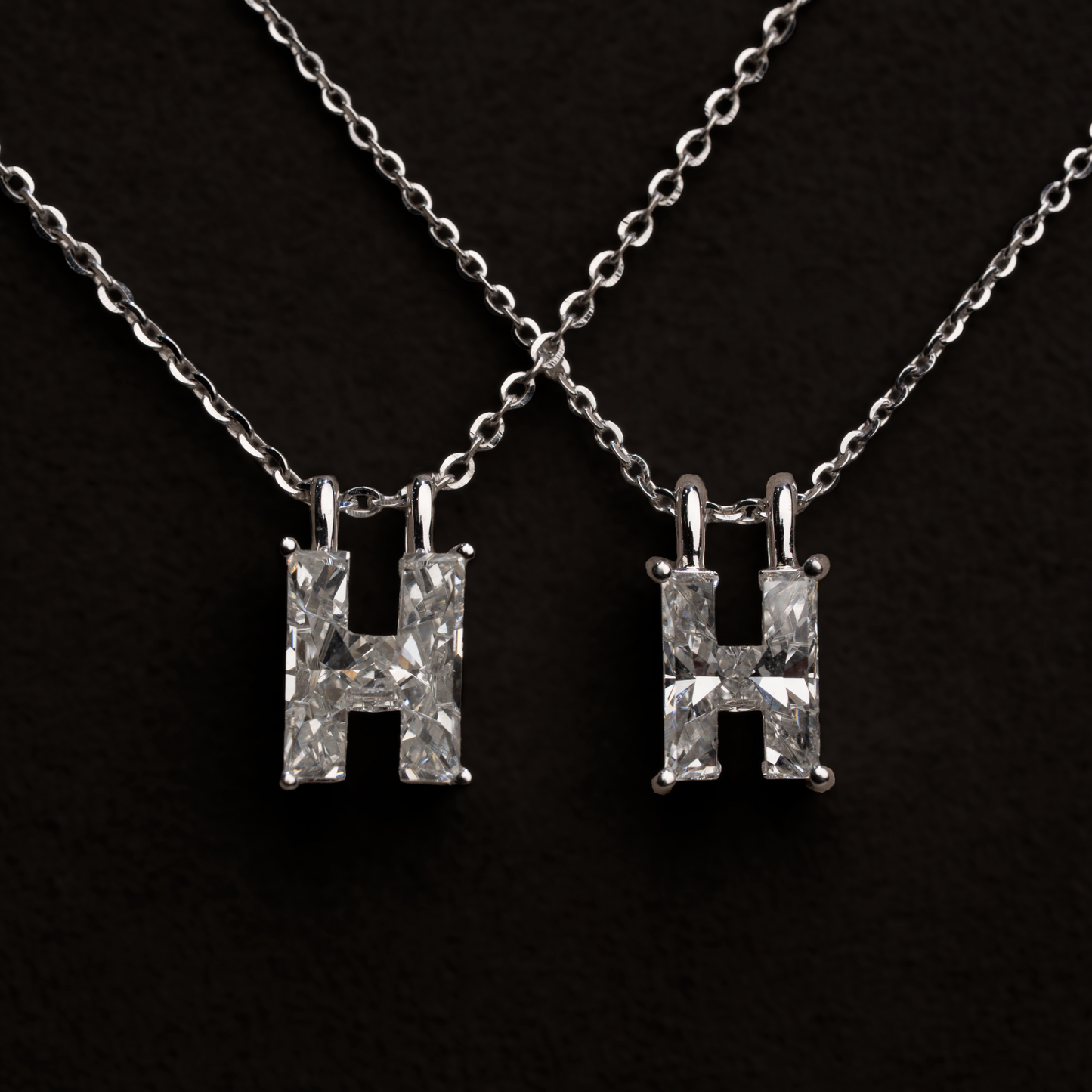 2 white gold necklaces with larger and smaller 'H' letter shaped single diamond pendants on a black background
