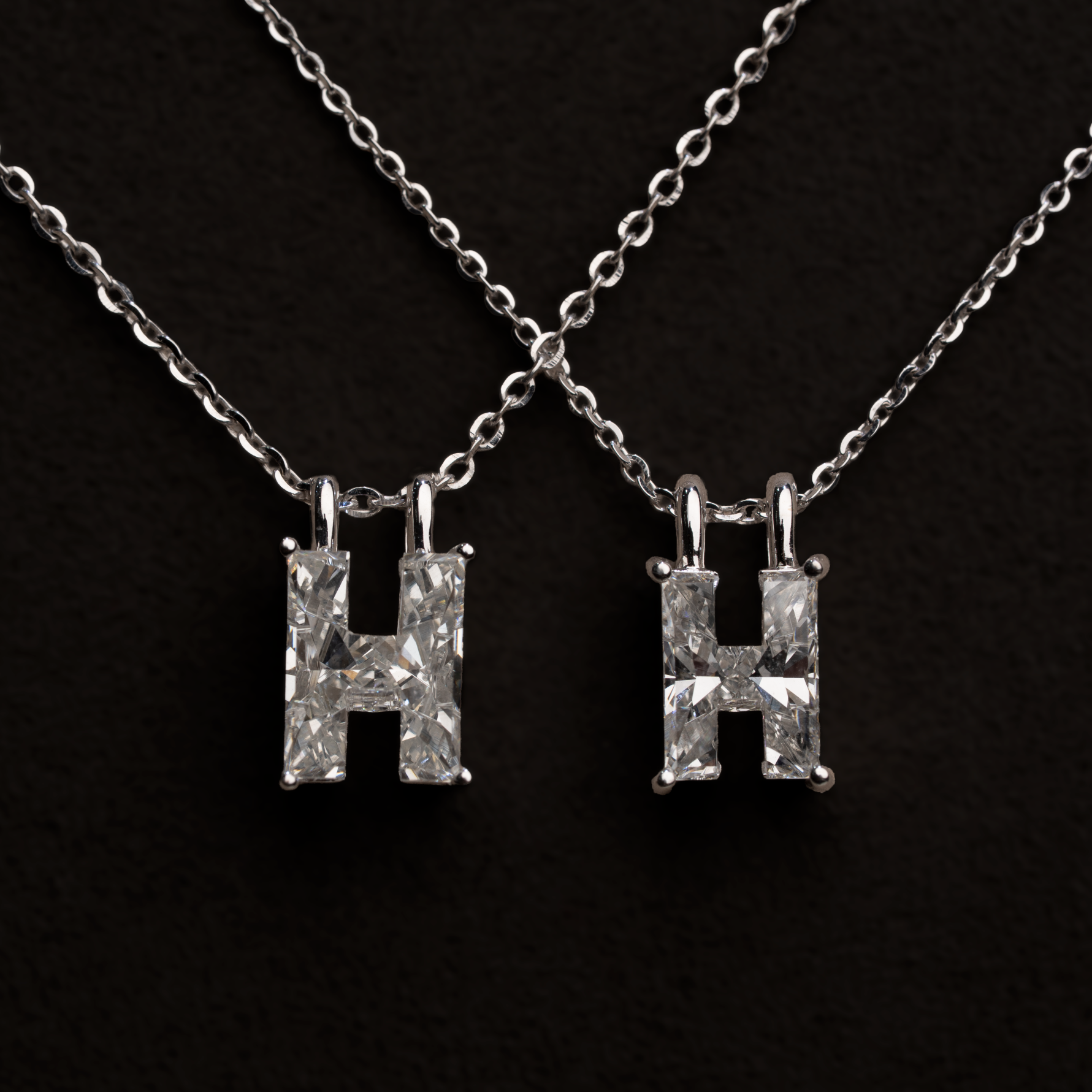 2 white gold necklaces with larger and smaller 'H' letter shaped single diamond pendants on a black background