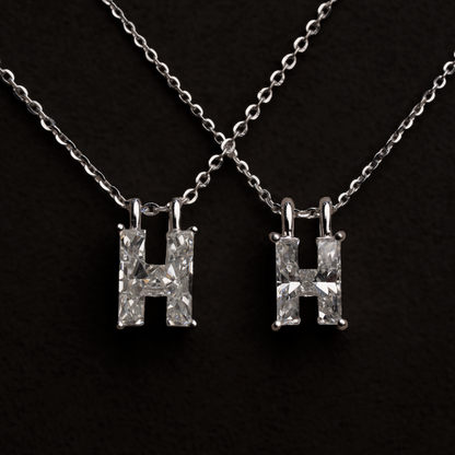 2 white gold necklaces with larger and smaller 'H' letter shaped single diamond pendants on a black background
